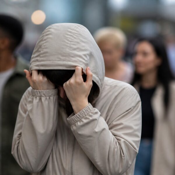 Pessoa trans protegendo seu rosto em um ambiente urbano, simbolizando privacidade e respeito.