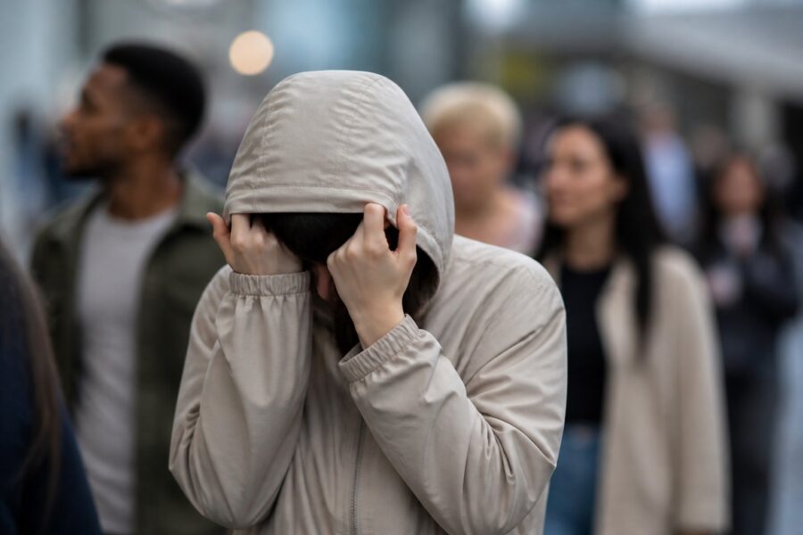 Pessoa trans protegendo seu rosto em um ambiente urbano, simbolizando privacidade e respeito.